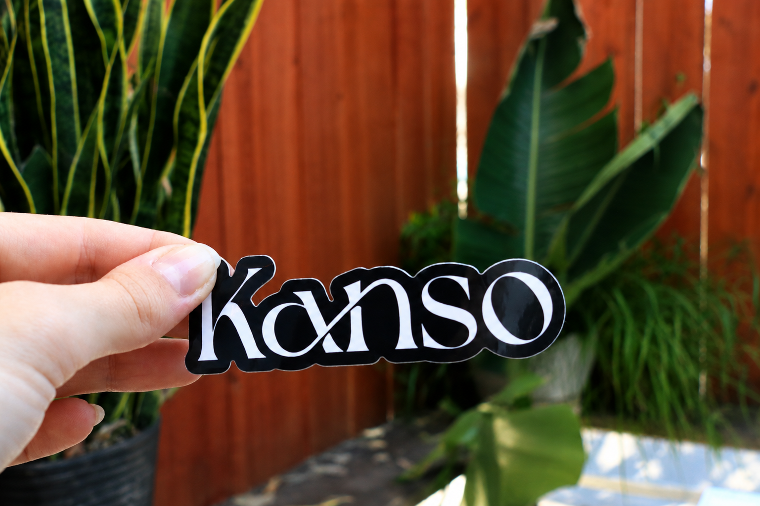 A Kanso sticker held up against a sunny fence